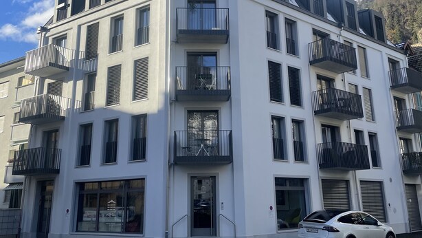 Een modern meerhooggezinsgebouw met balkons, een auto ervoor en een heldere lucht.