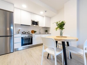 A modern kitchen with white cabinets, stainless steel appliances, and a dining area with a wooden table and white chairs.
