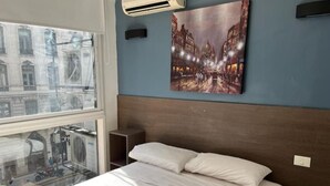 A hotel room with a bed, a window with a view of buildings, and a wall-mounted air conditioner. - Muy Bien Ubicado y Comodo (ABN)