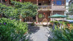 A traditional wooden house with a balcony, surrounded by lush greenery and potted plants. - fenghelijiang (Lijiang)