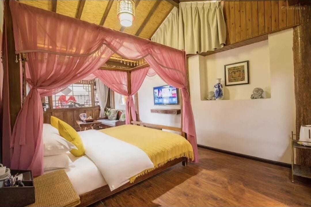 A bedroom with a four-poster bed, wooden flooring, and a television in the background.