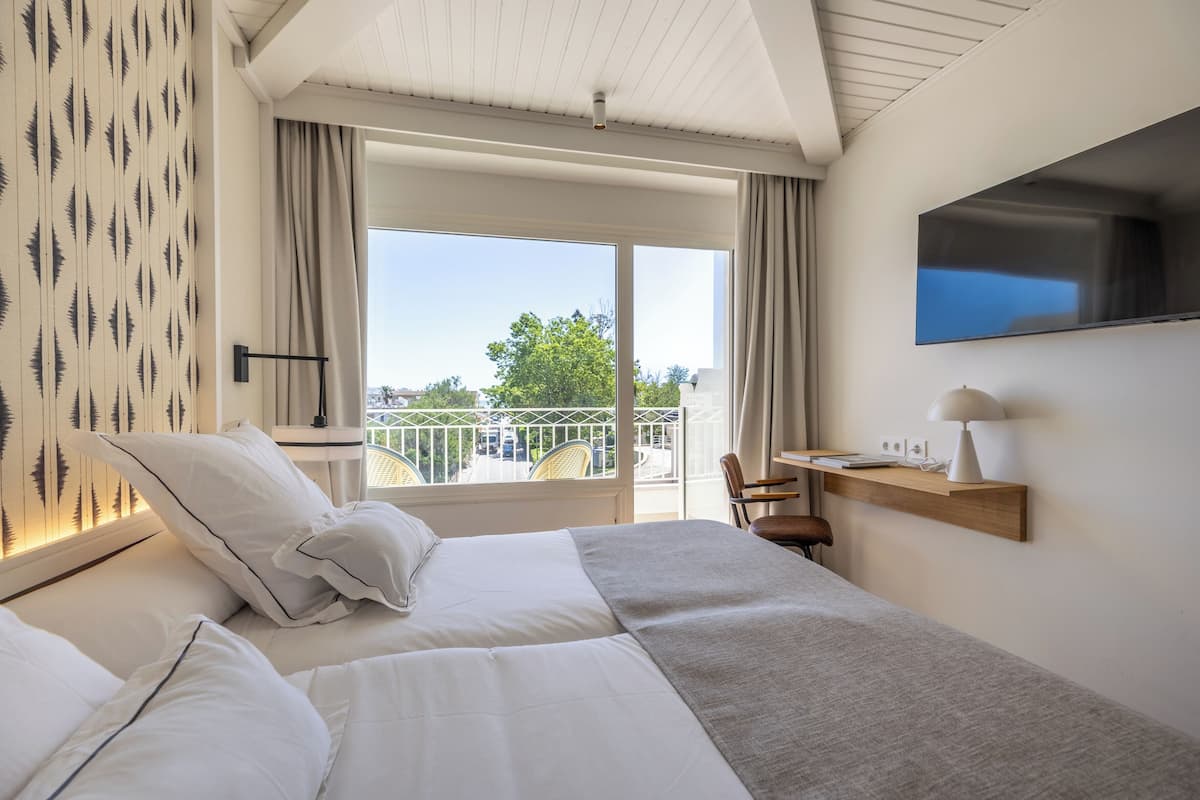 A hotel room with a bed, a desk, a TV, and a balcony with a view.