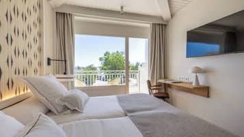 Quarto de hotel com cama, escrivaninha, televisão e varanda com vista.