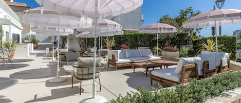 A patio area with outdoor seating, umbrellas, and a view of the sea.