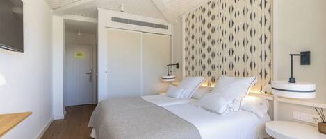 Un dormitorio con cama, mesitas de noche, un televisor montado en la pared y una puerta que da a otra habitación.
