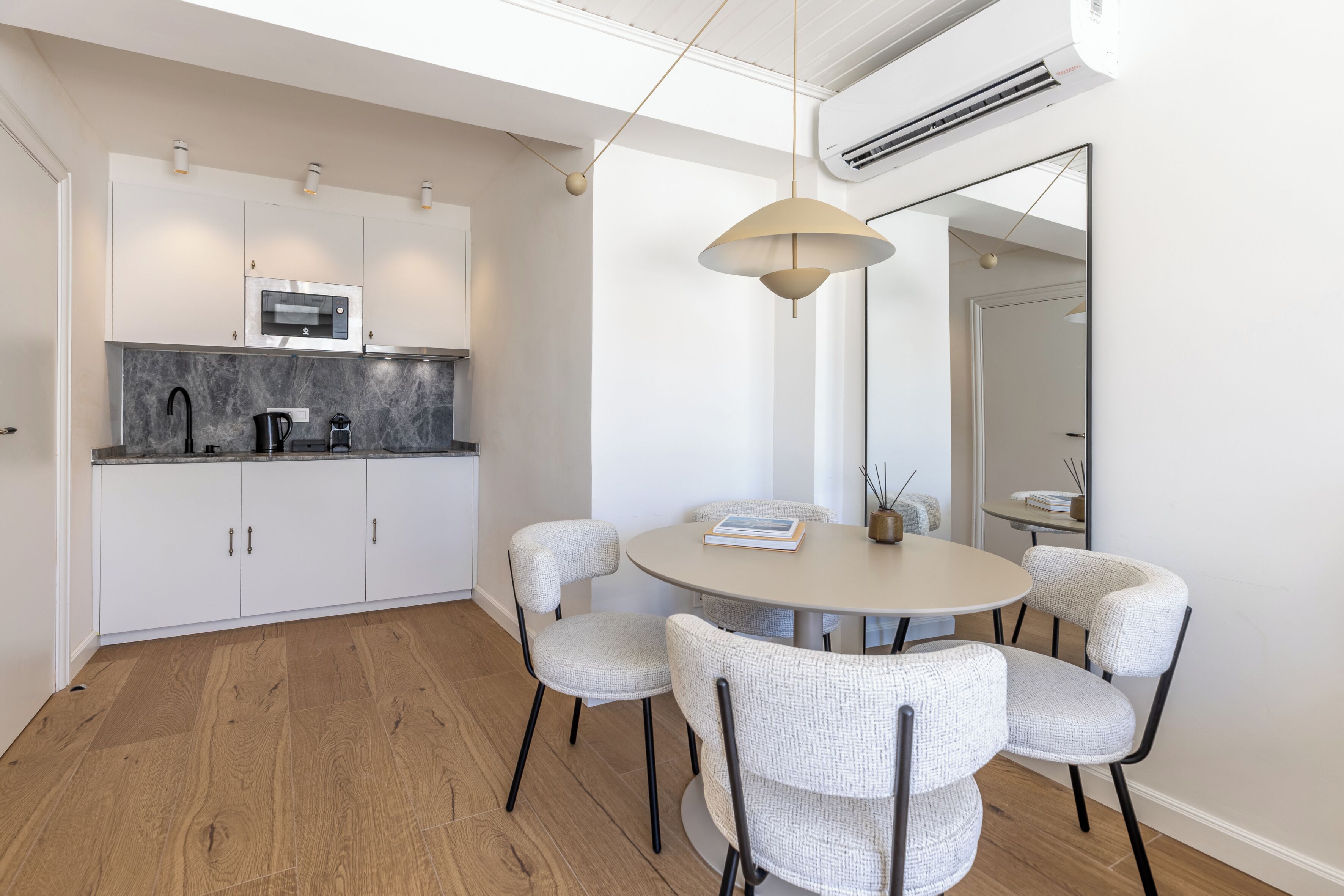 A modern kitchen with white cabinetry, a built-in microwave, and a round dining table with four chairs.