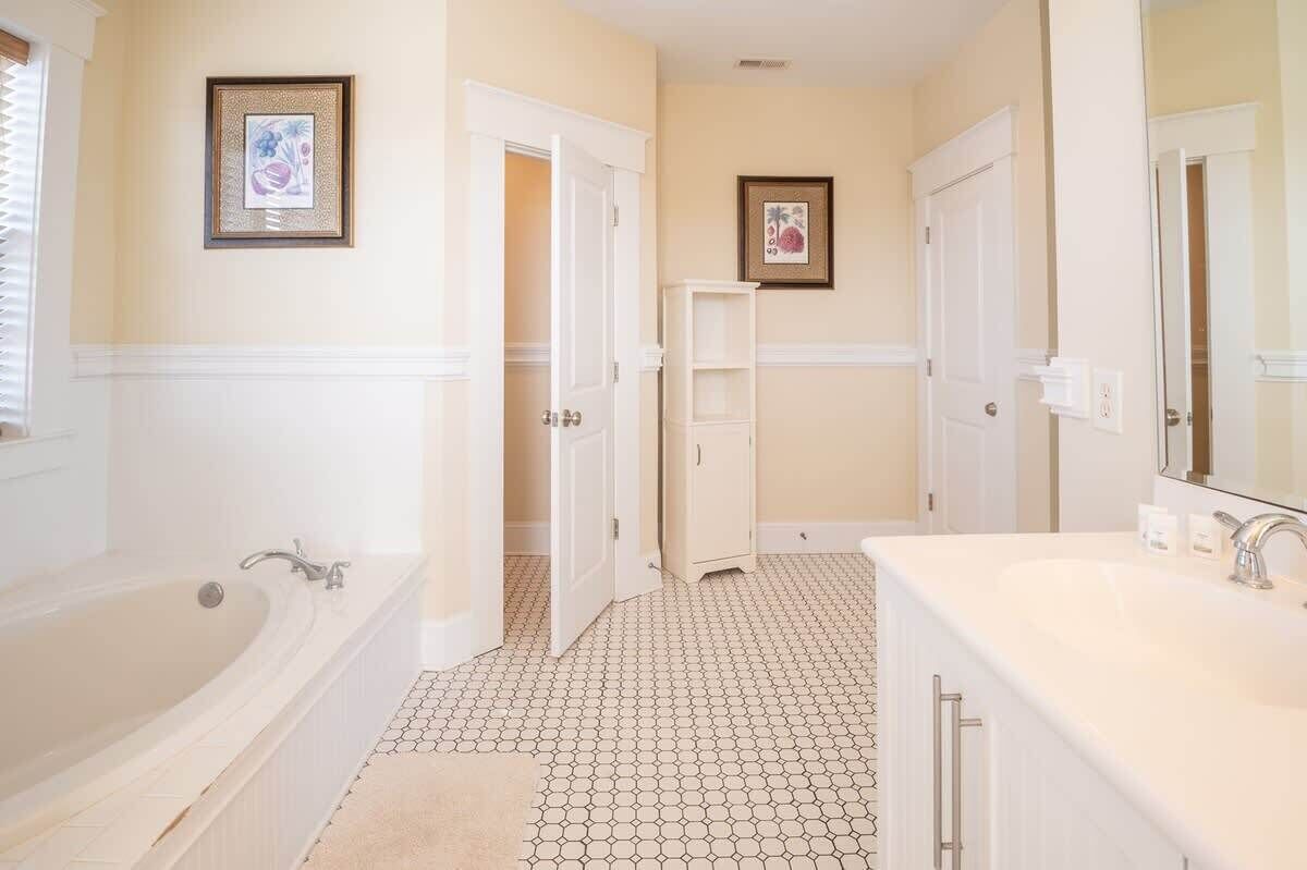 A bathroom with a bathtub, a sink, and two doors leading to other rooms.