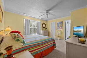 A hotel room with a bed, a desk, a television, a ceiling fan, and a window with curtains.