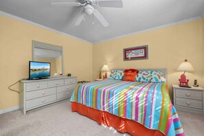 Quarto com cama, ventilador de teto, televisão e cômoda.