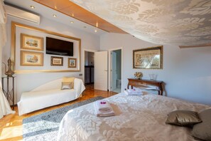 Een slaapkamer met een bed, een witte bank, een houten dressoir en een grote spiegel.