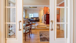 Une porte ouverte donne sur un salon aménagé avec un canapé, des fauteuils et un téléviseur.