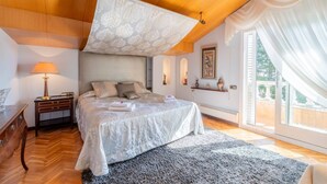 Une chambre avec un grand lit, une table de chevet, une lampe et une vue sur l’extérieur.