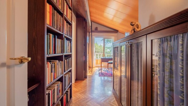Un couloir avec des étagères à livres, un plafond en bois et une vue sur un espace extérieur aménagé avec une table et des chaises.