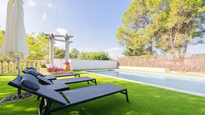 Un espace aménagé au bord de la piscine, avec une pelouse artificielle, des chaises longues et une pergola.