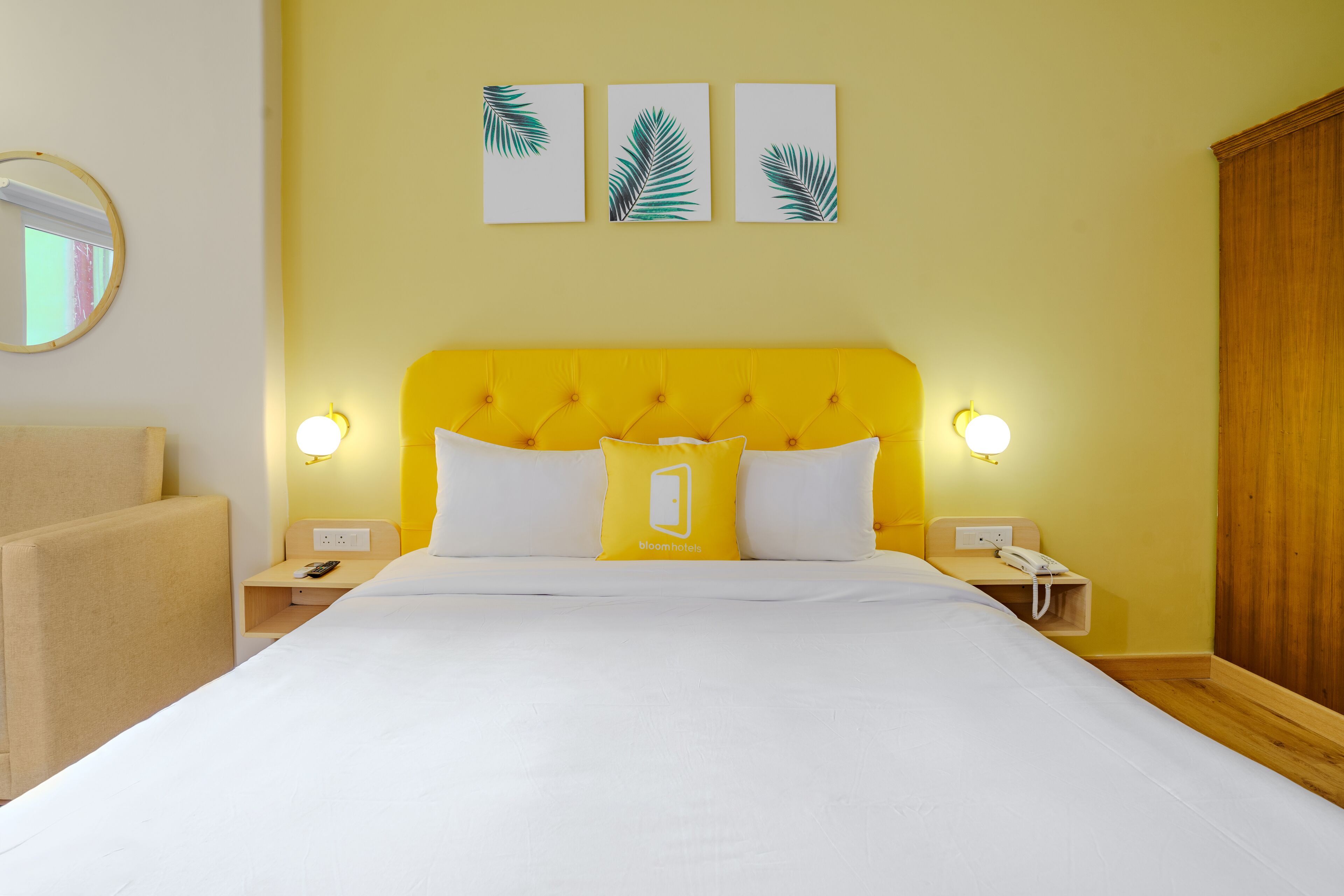 Habitación de hotel con cabecera amarilla, ropa de cama blanca y mesita de noche con teléfono y lámpara.