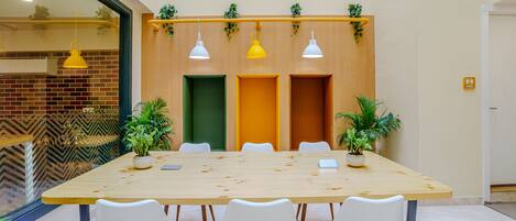 Un salón de conferencias con una larga mesa, sillas blancas y plantas en macetas.