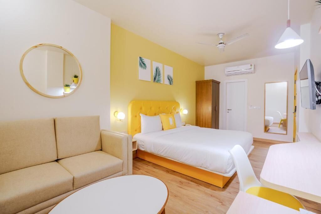 A hotel room with a bed, a sofa, a round table, and a mirror.