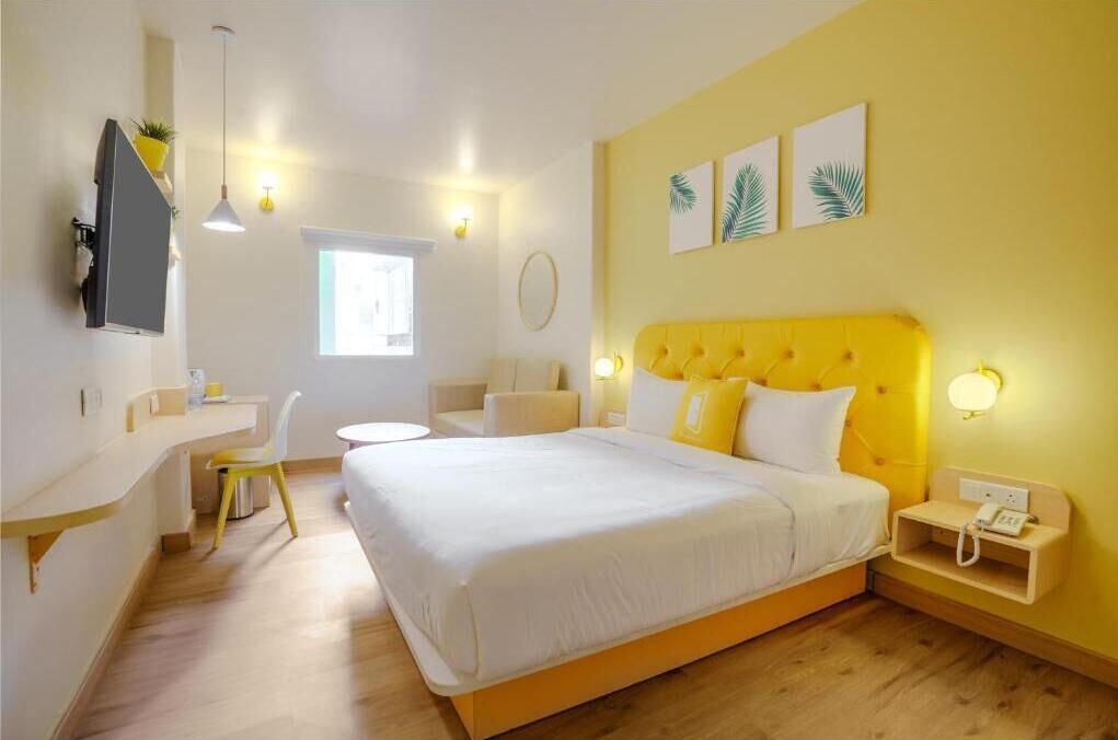 A hotel room with a bed, bedside table, chair, desk, and a TV mounted on the wall.