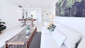 A modern living room with a white sofa, a glass coffee table, and a dining area with clear chairs. - le cartier sunny isles ocean paradise (Sunny Isles Beach)