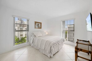 Ein Schlafzimmer mit einem Bett, einem Bild an der Wand und einem Fenster mit Blick auf Gebäude.