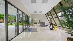 A modern lobby with glass doors, a reception desk, and a large window with a view of greenery. - le cartier sunny isles ocean paradise (Sunny Isles Beach)