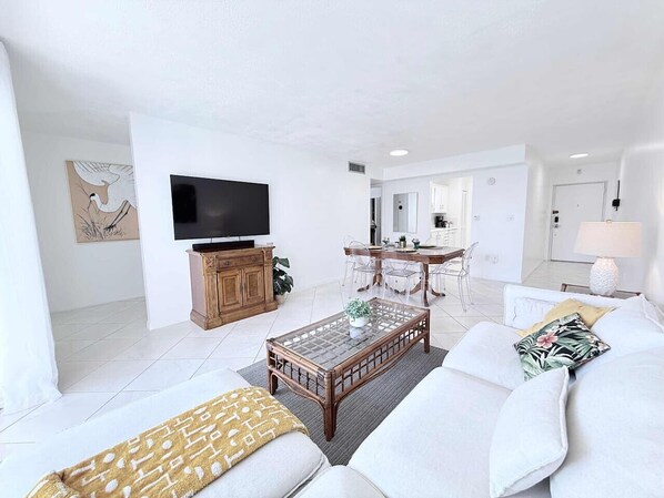 Ein modernes Wohnzimmer mit Flachbildfernseher, Couch, Holztisch und Essbereich mit Stühlen und Tisch.