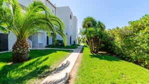 A white building with a pathway leading to the entrance, surrounded by lush green grass and palm trees. - Parque Mar Apartments (Santanyi)