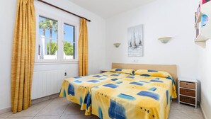 A bedroom with two beds, a window with curtains, a nightstand, and a wall-mounted shelf. - Parque Mar Apartments (Santanyi)