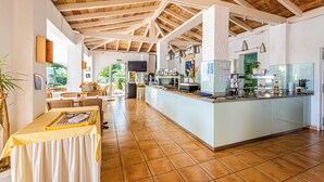 A spacious kitchen with a high ceiling, a central island with a sink, and a dining area with tables and chairs. - Parque Mar Apartments (Santanyi)