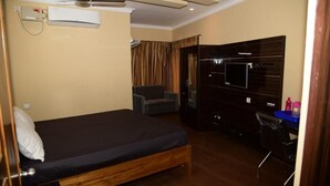 Un dormitorio con cama, una silla, un escritorio, un televisor y un aire acondicionado.
