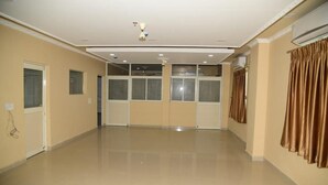 Una habitación amplia con piso pulido, ventilador de techo y un gran ventanal con persianas.