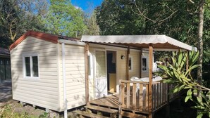 A small, single-story cabin with a porch and a covered outdoor seating area. - Mobile home Trigano 5 people AIR-CONDITIONED (ST JEAN DE VALERISCLE)