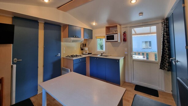 A compact kitchen with a gas stove, microwave, and sink. There is a small window with a view of a house outside. - Mobile home Trigano 5 people AIR-CONDITIONED (ST JEAN DE VALERISCLE)
