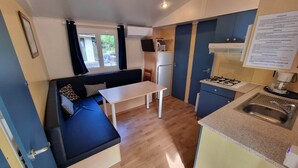 A compact kitchenette with a gas stove, sink, and a small dining table. - Mobile home Trigano 5 people AIR-CONDITIONED (ST JEAN DE VALERISCLE)