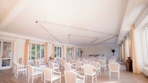 Une pièce spacieuse avec des rangées de chaises blanches et une longue table, de grandes fenêtres et un ventilateur de plafond.