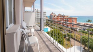 Un balcon avec des chaises blanches, une piscine bleue et une vue sur la mer et les bâtiments.
