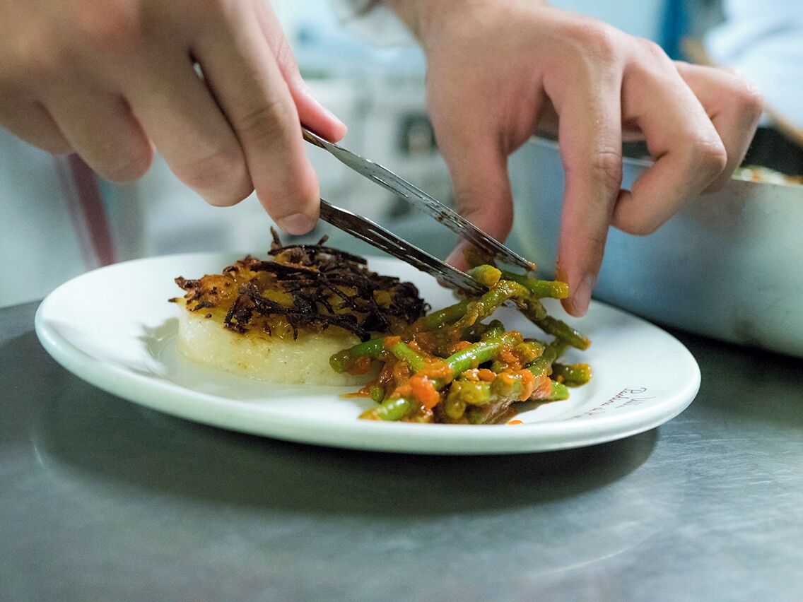Une personne utilise une pince pour servir de la nourriture d’une casserole et la déposer dans une assiette.