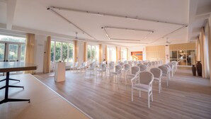 Une salle de conférence spacieuse, avec des rangées de chaises blanches, un pupitre et de grandes fenêtres donnant sur l’extérieur.