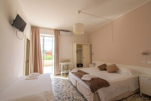 Hotellihuone, jossa on kaksi sänkyä, seinälle asennettu televisio, kattotuuletin ja näkymä ulos.