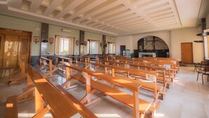 Un vaste intérieur d’église avec des bancs en bois disposés en rangées, un plafond élevé avec des poutres en croix et une grande fenêtre en arc de cercle.