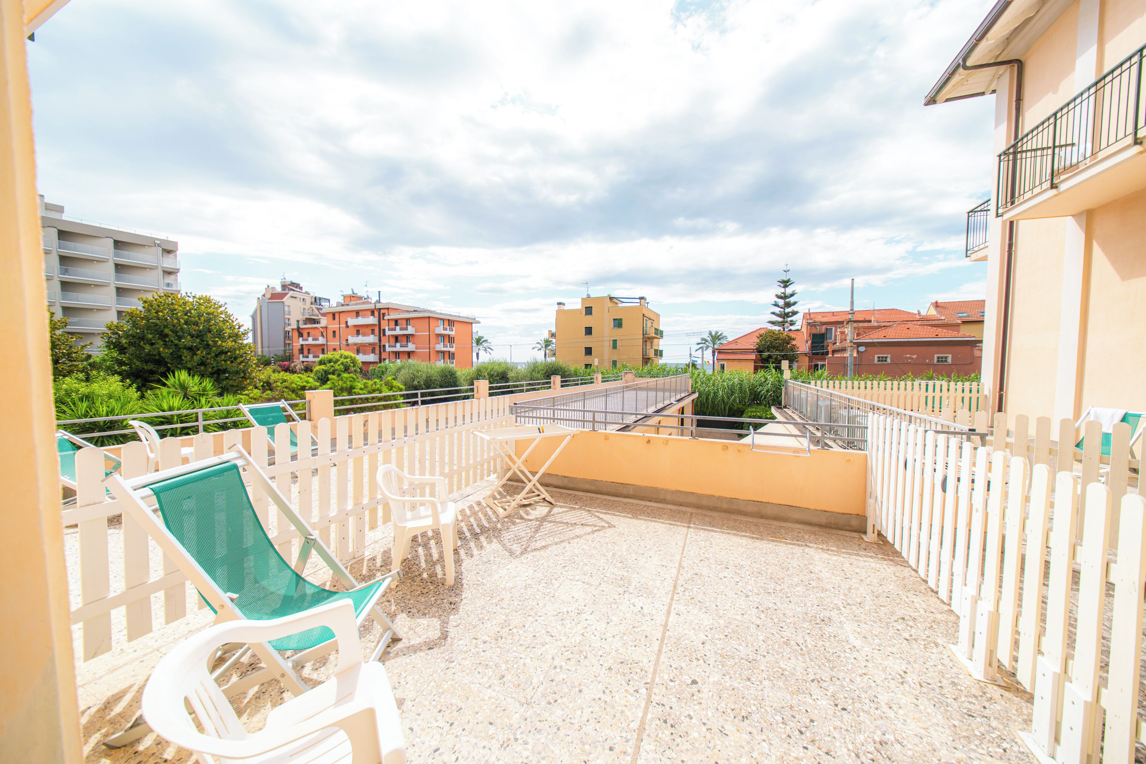 A balcony with a seating area, a view of surrounding buildings, and a clear sky.