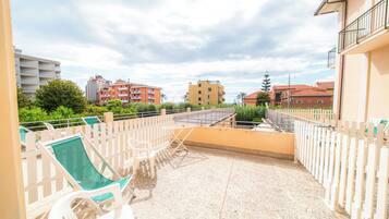 A balcony with a seating area, a view of surrounding buildings, and a clear sky.