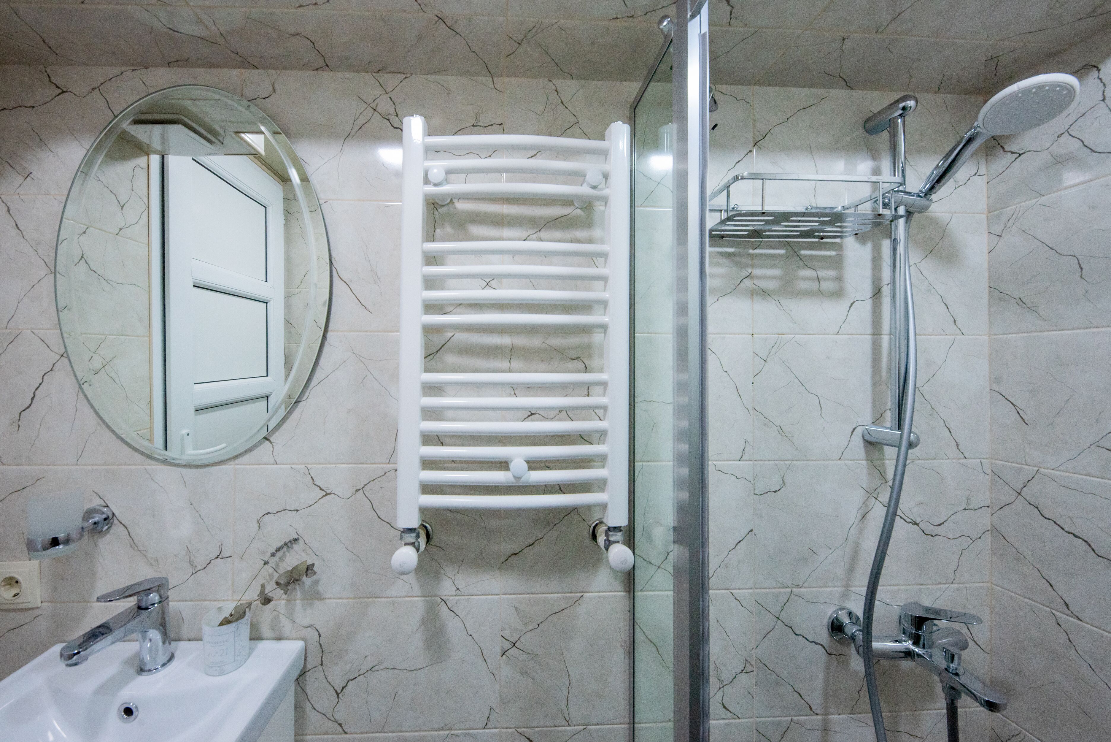 Un baño con un lavamanos blanco, un espejo, toallero, ducha y cabina de ducha con paredes de vidrio.