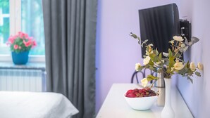 Et værelse med et hvidt bord, en hvid vase med blomster, en skål med frugt og et vindue med gardiner.