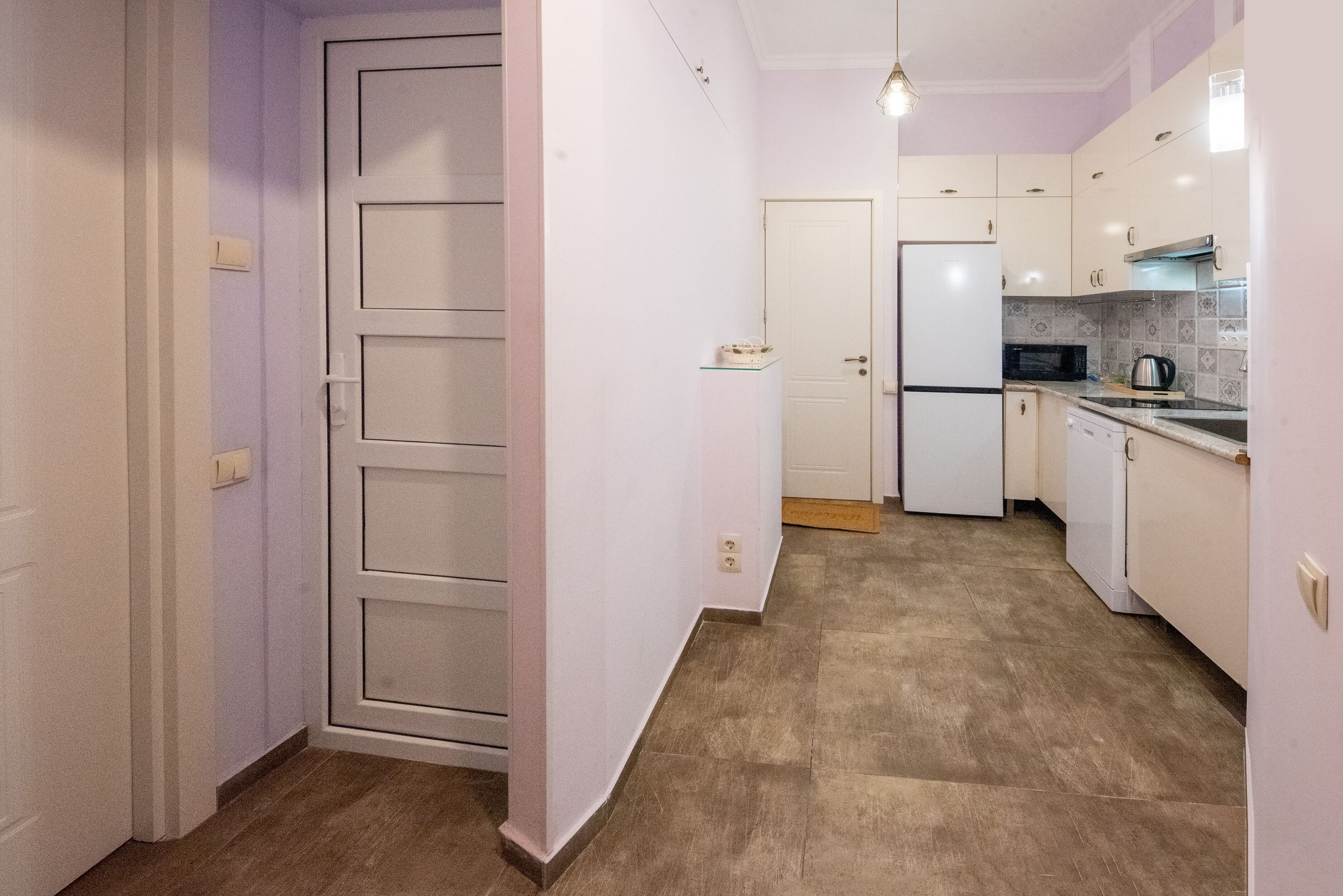A narrow hallway leading to a kitchen with a refrigerator, microwave, and stove.