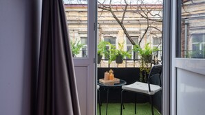 Et værelse med en skydedør, der fører ud til en balkon med kunstgræs, et lille bord med stole og plantekasser.