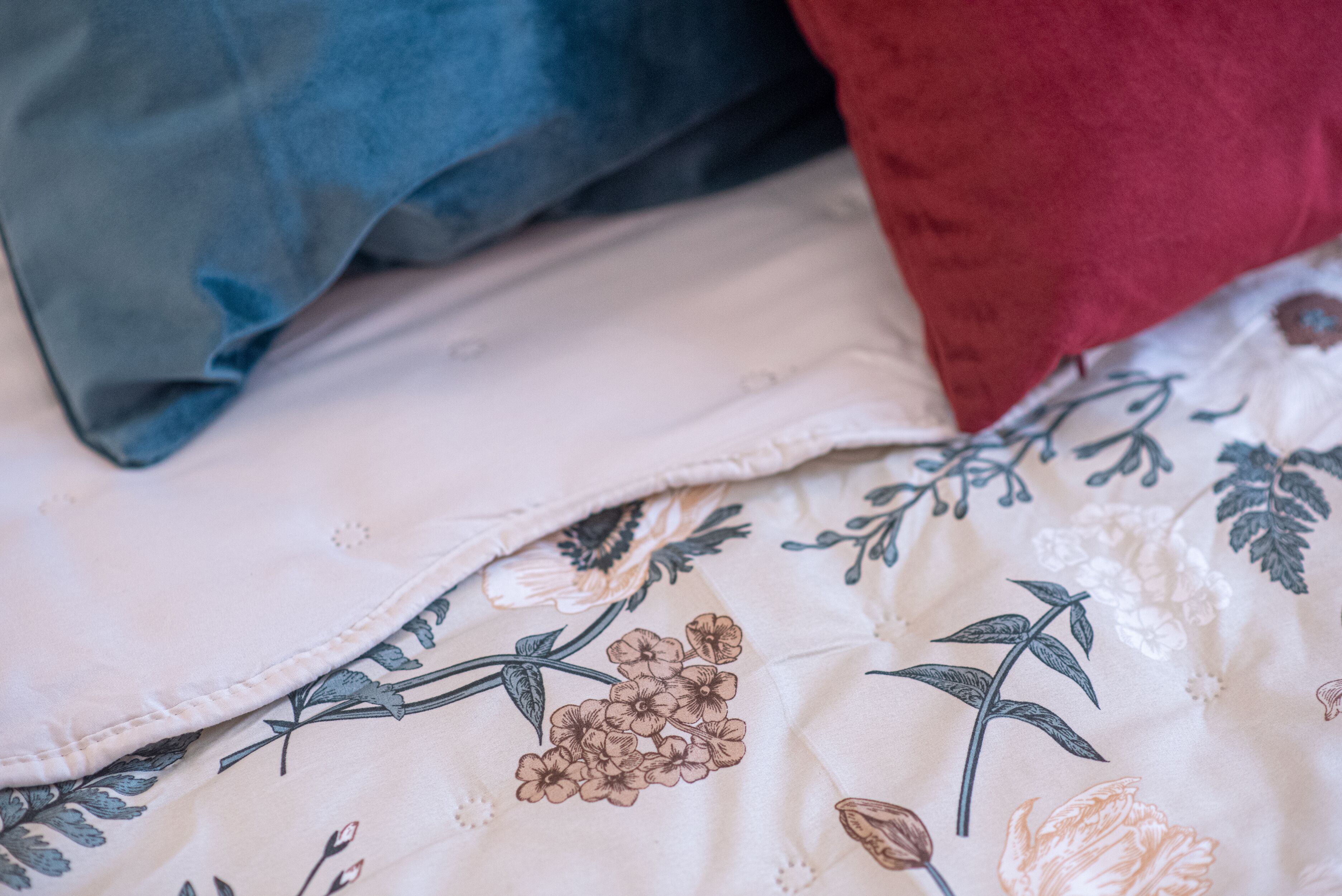 Un lit avec une couvre-lit à motifs floraux et des oreillers bleus et rouges.