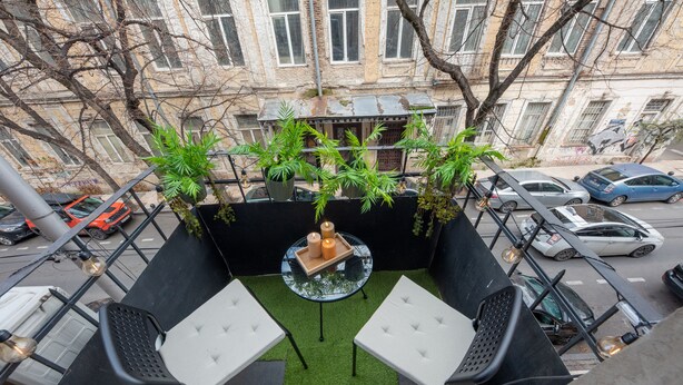 En balkon med to hvide polstrede stole, et lille rundt bord med bakke, og grønne planter.