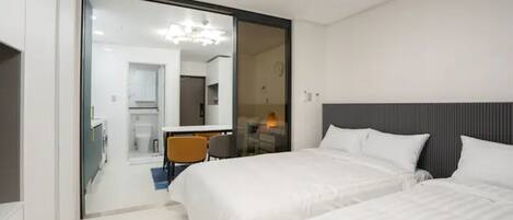 Quarto de hotel moderno com duas camas, porta de vidro para uma cozinha compacta e uma pequena área de refeições.