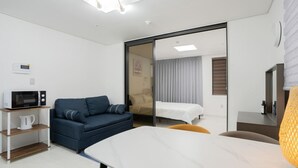A modern hotel room with a sofa, a bed, a desk, a microwave, and a lamp.